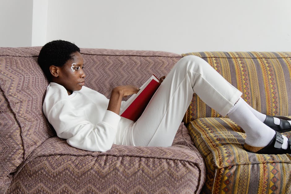 Woman relaxing and reading a book on a cozy sofa indoors, conveying solace and personal time.
