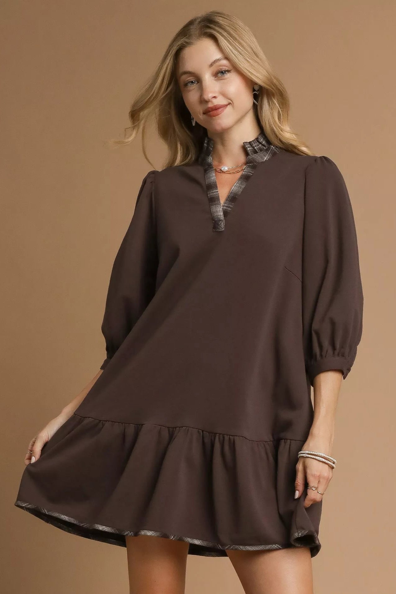 Woman wearing a brown dress with a fur collar against a beige background